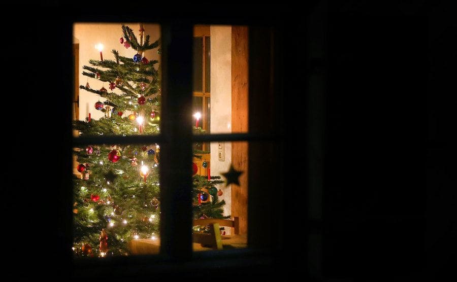 A decorated Christmas tree lights up behind the window of a house.