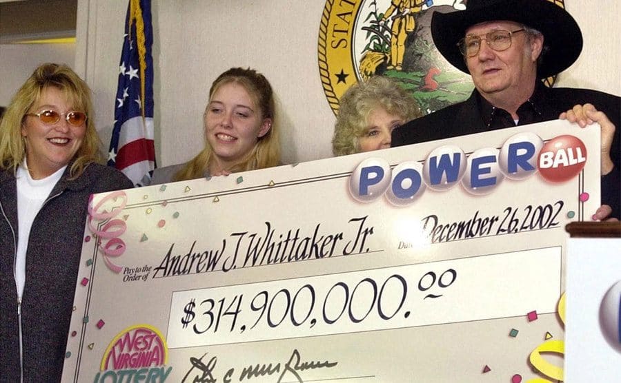 Whittaker and his family are holding his check after winning the Powerball lottery.