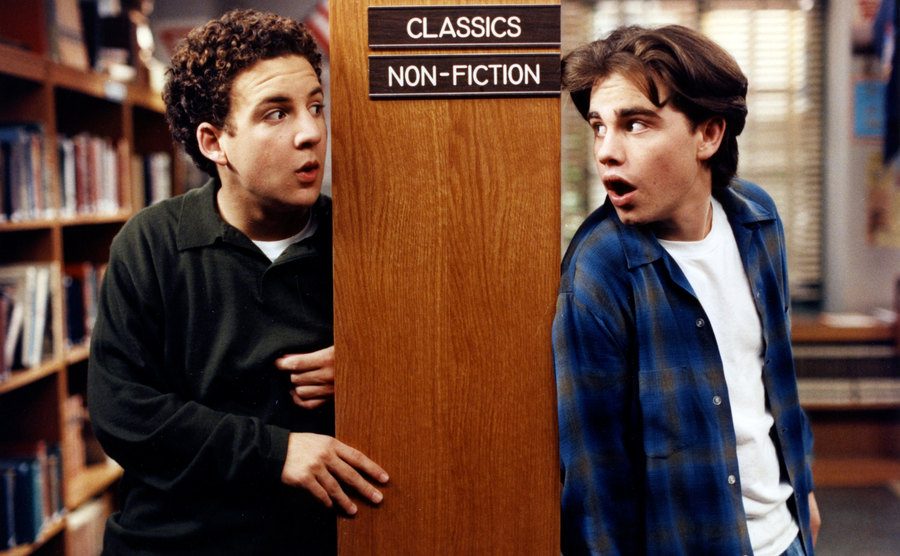 Cory and Shawn are sneaking around the library in a still from Boy Meets World. 