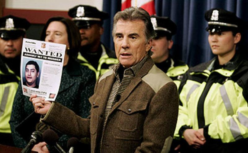 An image of John Walsh and surrounded by officers during a press conference.
