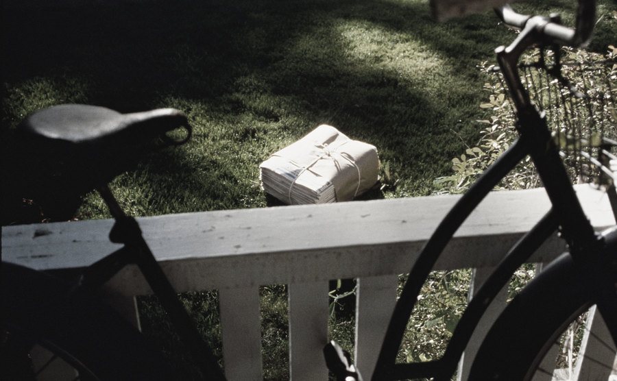 A picture of a bike, a bundle of newspapers, and a yard.