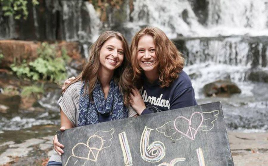 A picture of Sarah and Jennifer celebrating their love carrying a positive sign.