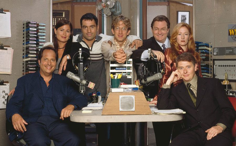 The cast of NewsRadio pose together on set.