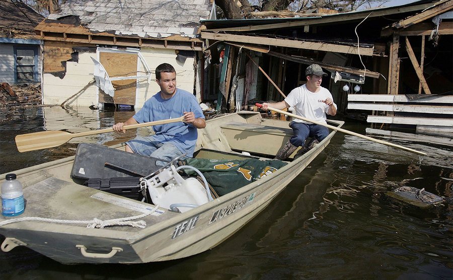 Two men are paddling in a boat after the hurricane. 